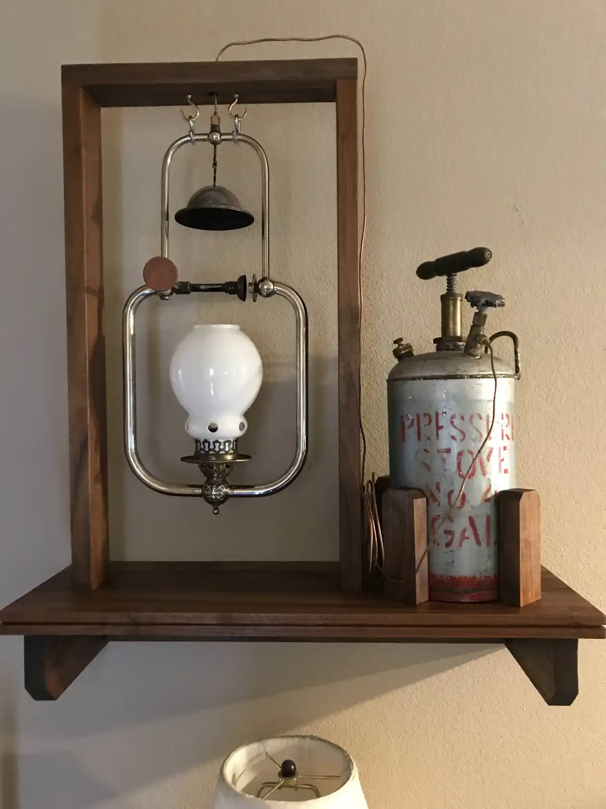 A vintage-style oil lamp with a white glass globe and metal frame is mounted inside a wooden shelf frame, connected by wires…