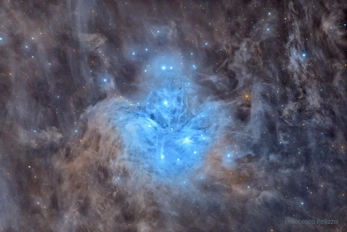 A stunning astrophotograph of a cosmic nebula, featuring swirling clouds of gas in shades of blue and brown, illuminated by…