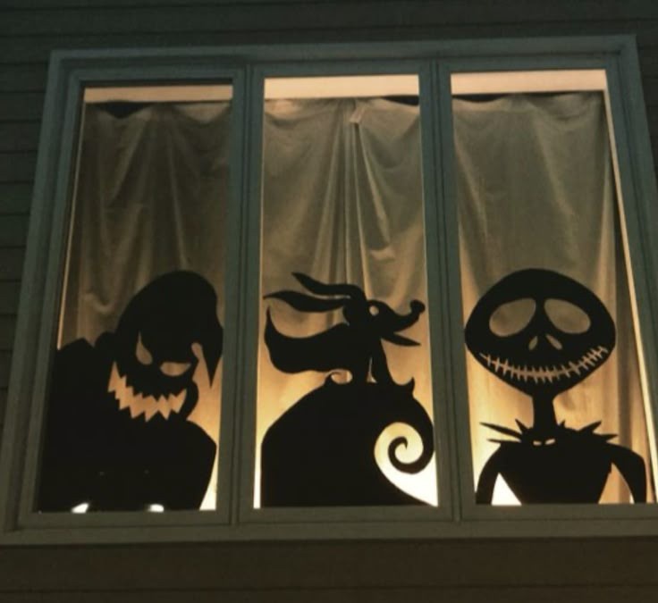 Three black silhouette cutouts of characters from The Nightmare Before Christmas are taped to a window, visible against the…