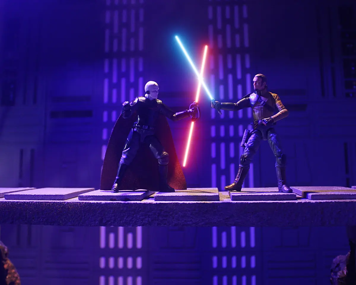 Two Star Wars action figures, one with a red lightsaber and one with a blue lightsaber, are locked in a lightsaber duel on a…