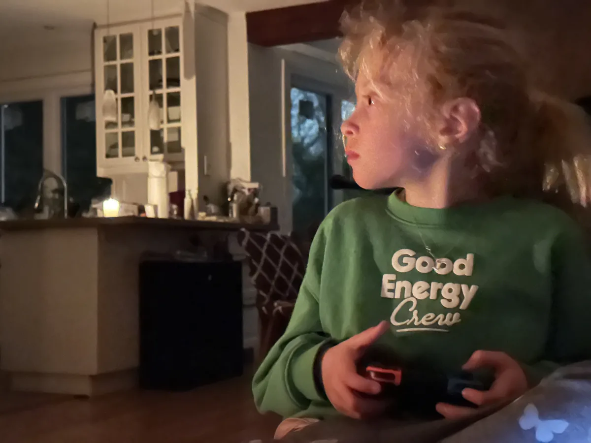 A young child with curly hair, wearing a green sweatshirt that reads 'Good Energy Crew', is shown in profile holding a video…