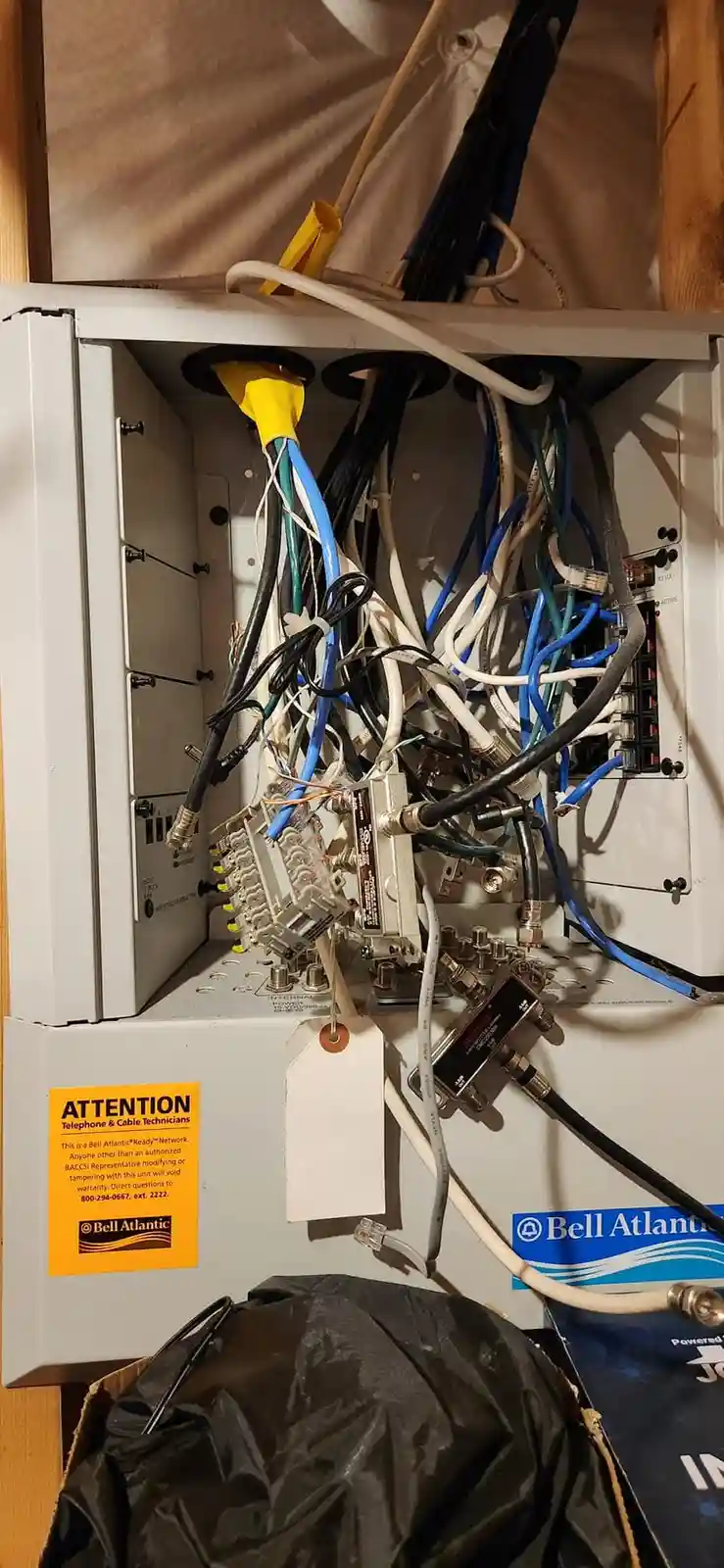 A messy, tangled mess of cables and wires inside a Bell Atlantic network equipment box, with a yellow warning label that…