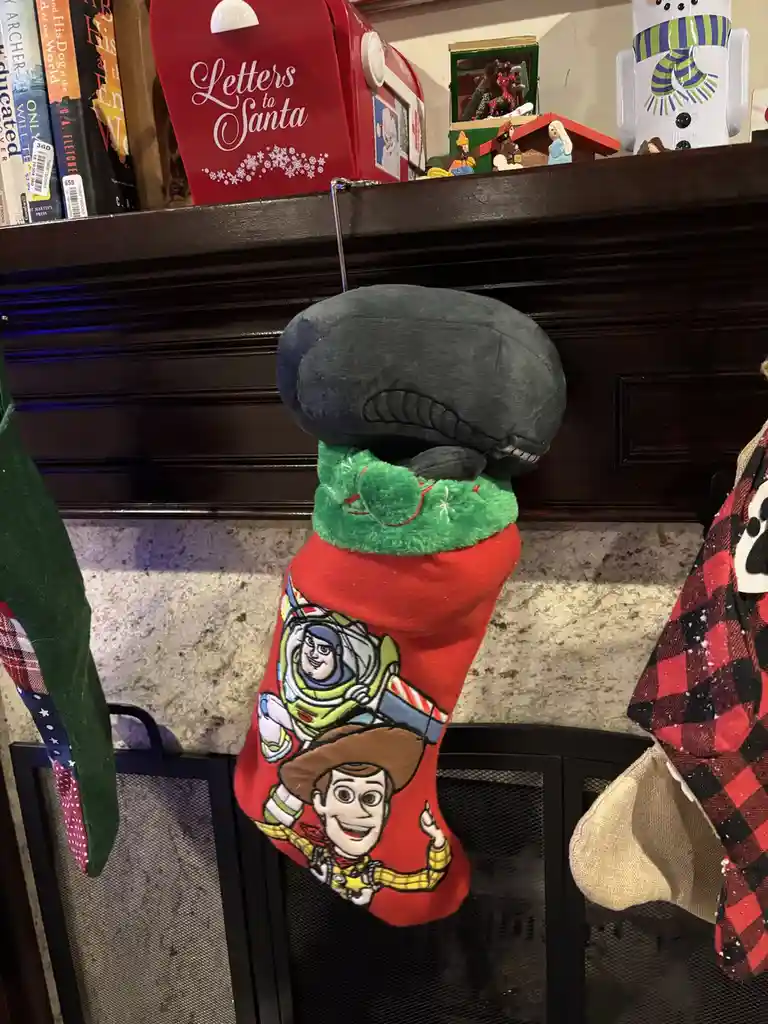 A red Christmas stocking featuring Toy Story characters Woody and Buzz Lightyear hangs on a fireplace mantle. The top of the…