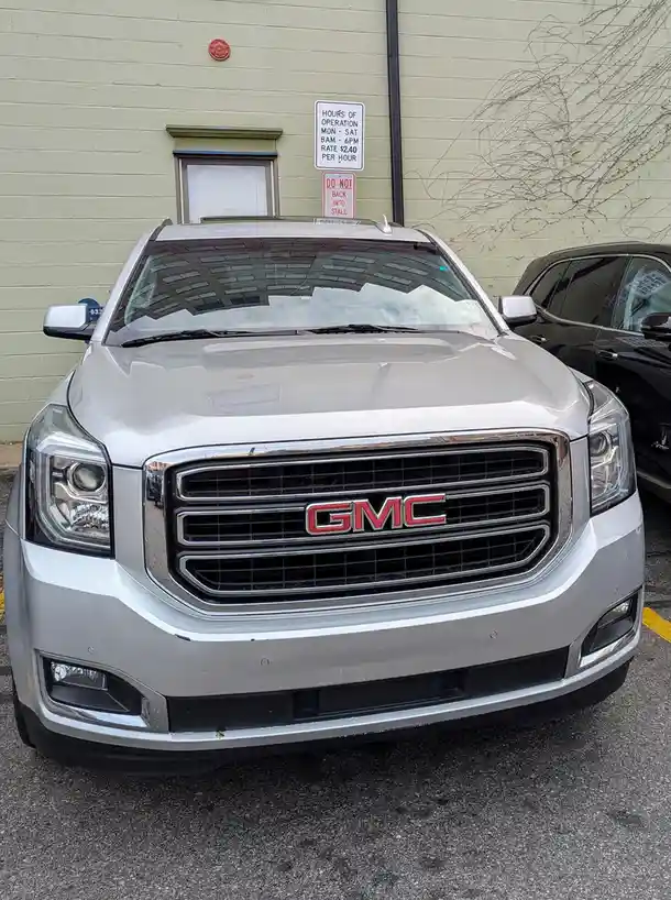A silver GMC SUV is parked in front of a building with a sign that reads 'DO NOT BACK INTO STALL' directly above the…