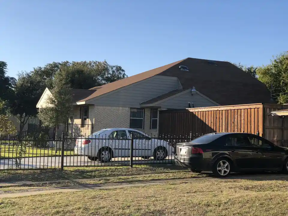 A suburban house with a brown shingled roof that has an unusual dome-like curvature, making it appear rounded instead of…