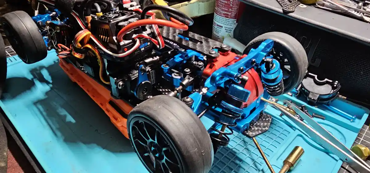 A close-up photo of a detailed radio-controlled car's chassis, showing its blue and orange mechanical components, black…