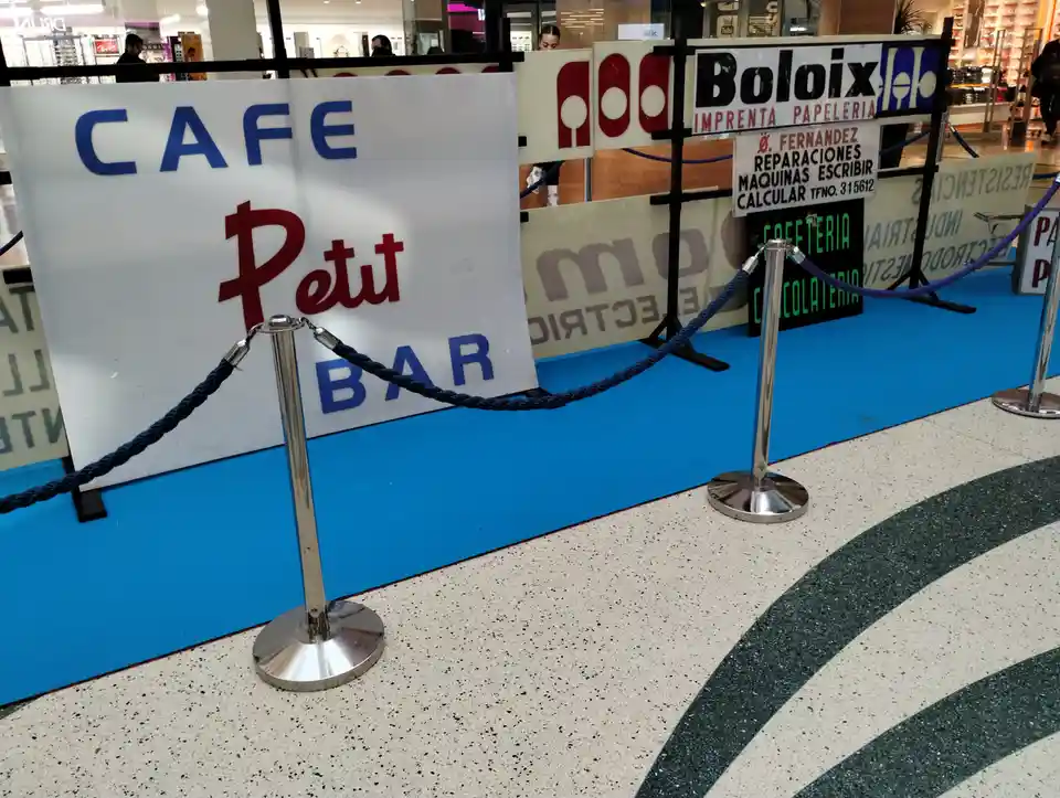 A photo of a mall or shopping center interior showing a 'CAFE Petit BAR' sign behind a blue carpet and stanchion ropes…