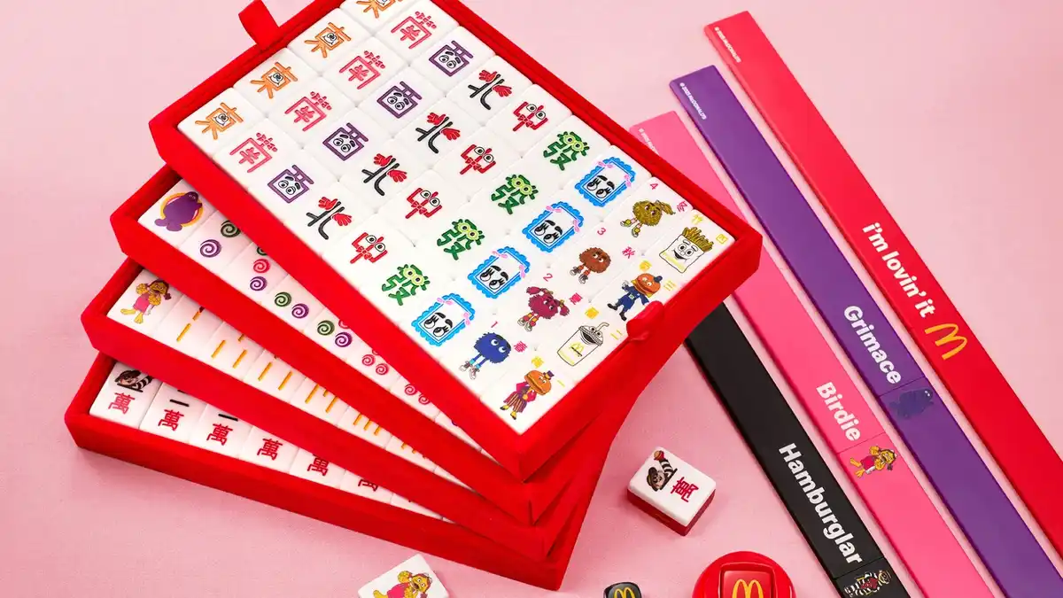 A promotional image displays three stacked red velvet boxes filled with colorful, cartoon-themed mahjong tiles featuring…