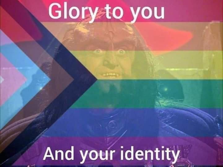 A close-up image of a character with a shocked or intense facial expression, overlaid with a rainbow flag pattern and a…