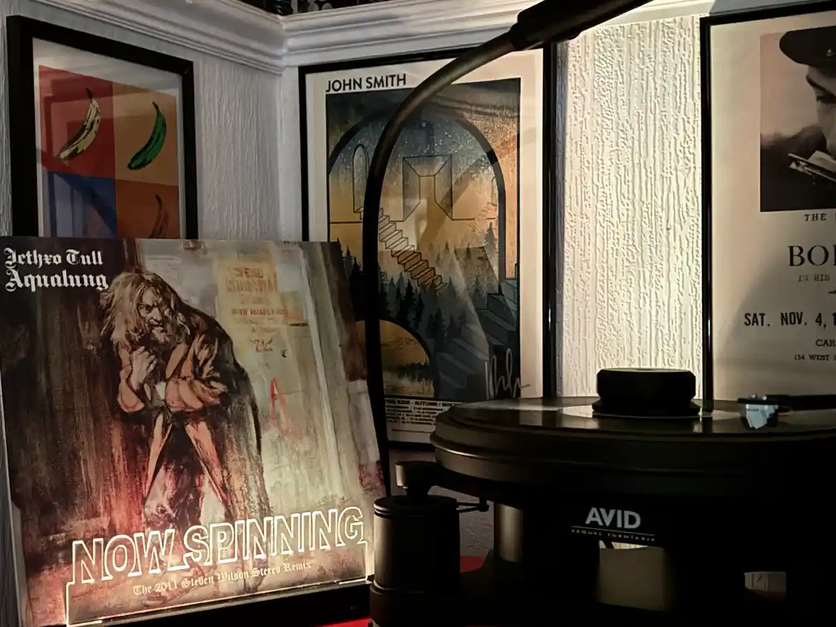 A close-up of a vinyl record player with an 'AVID' logo, positioned in front of framed posters including one for 'Jethro…