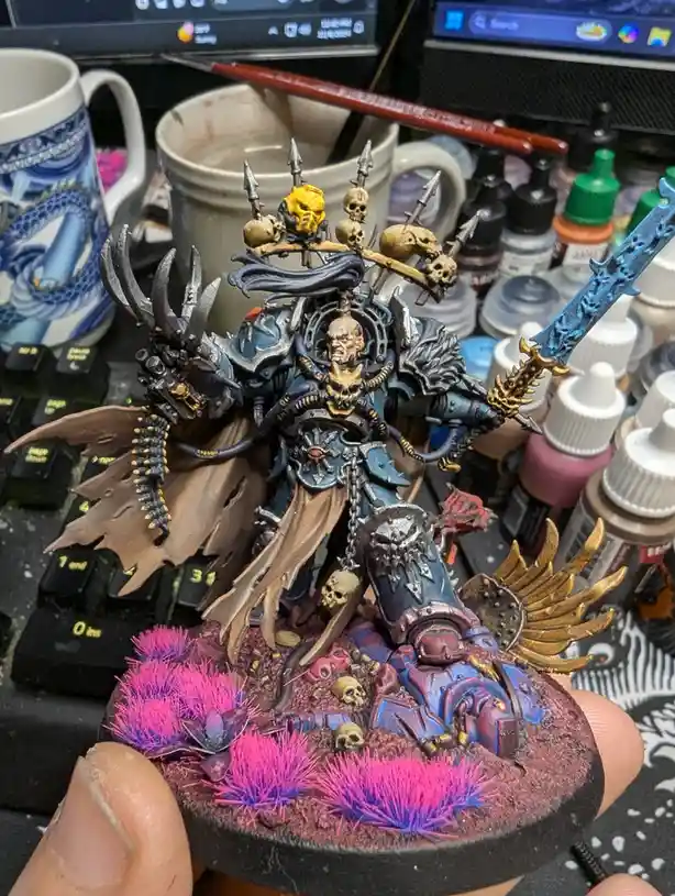 A highly detailed, painted miniature of a dark fantasy warrior with skulls, horns, and a blue sword stands on a base with…