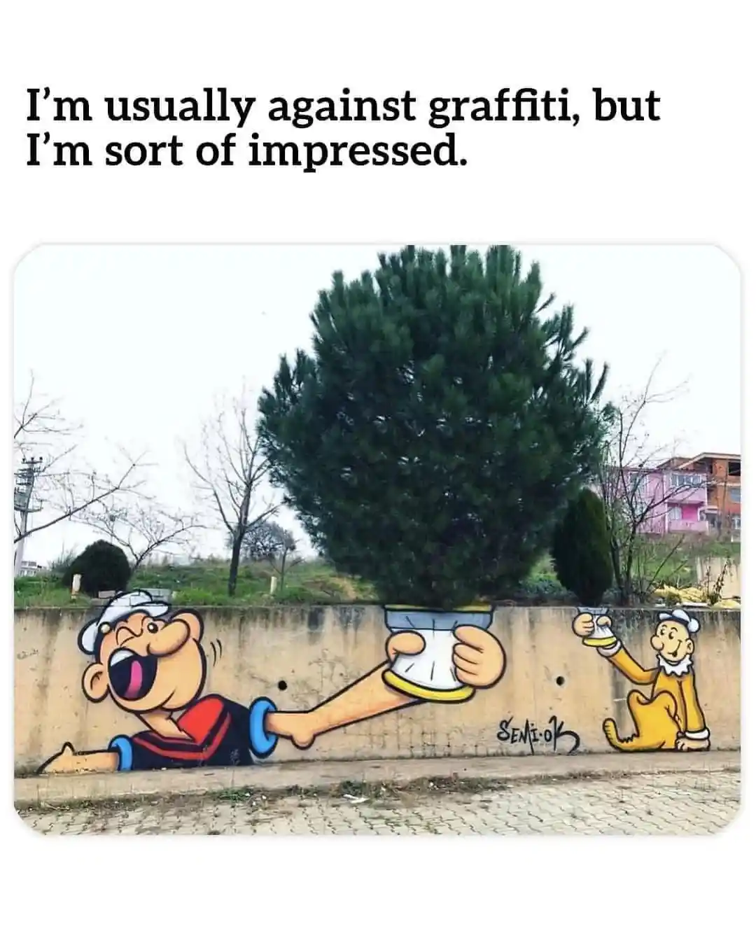 A photo of a concrete wall with a 3D graffiti mural of Popeye and Bluto. Popeye's arm extends from the wall, holding a…