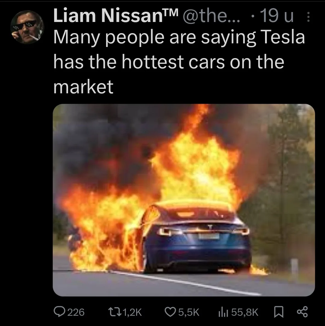 A blue Tesla car is engulfed in large flames and thick black smoke while driving on a road, with trees visible in the…