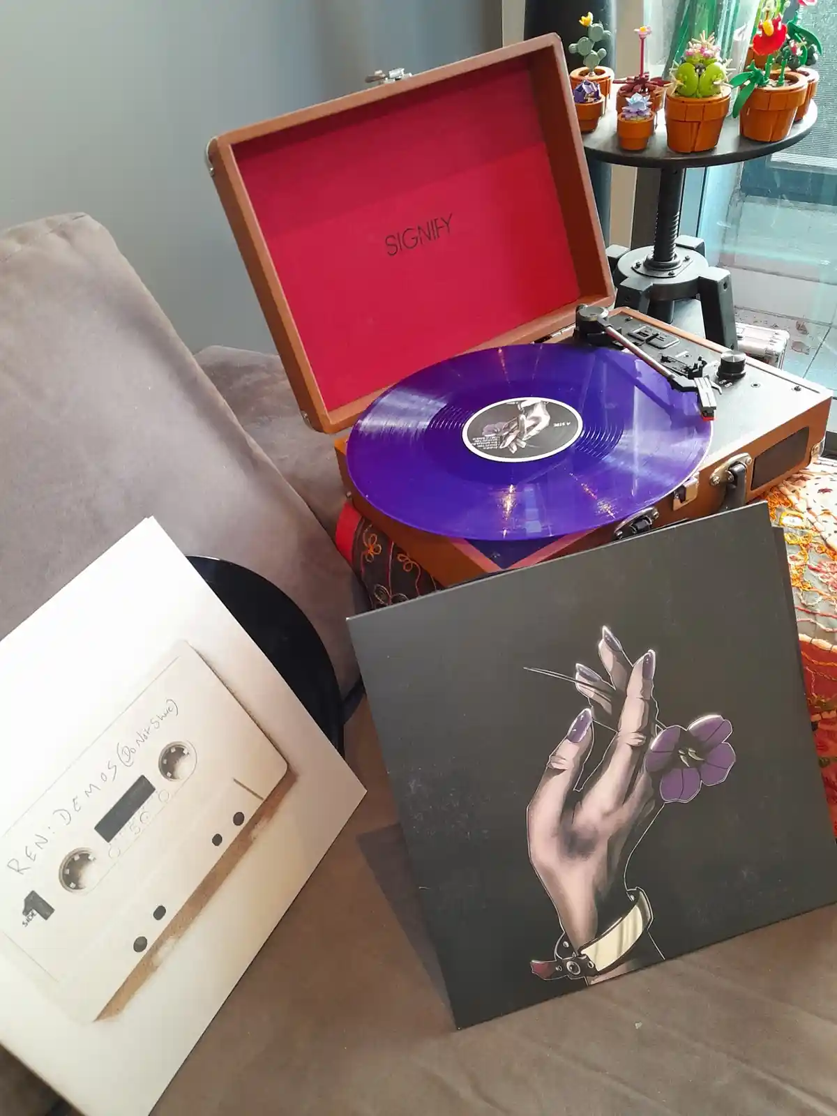 A purple vinyl record spins on a brown portable record player with 'SIGNIFY' written on its red interior lid. Beside it lies…