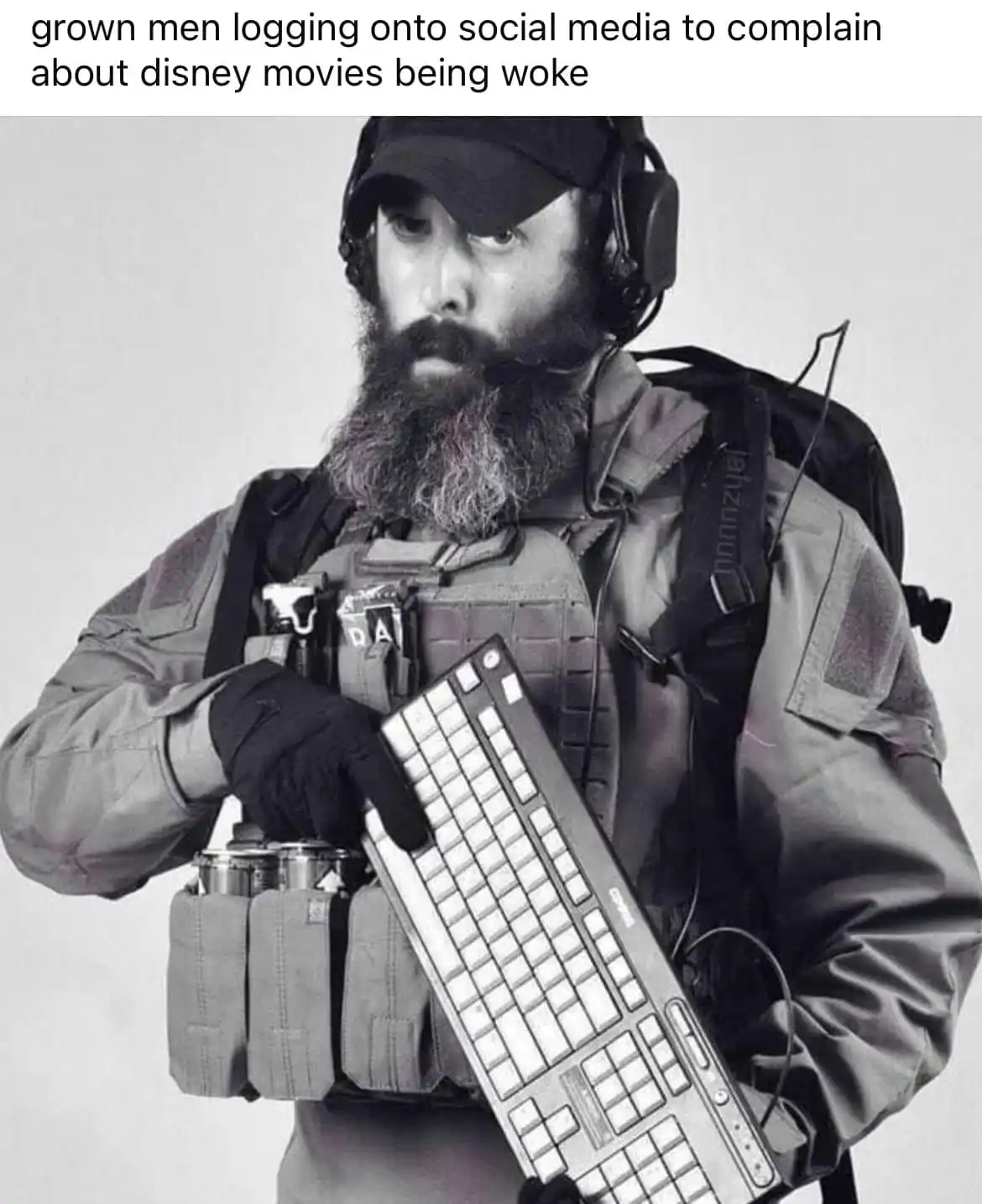 A black-and-white photo shows a bearded man in tactical gear, including a vest, backpack, and headset, holding a computer…