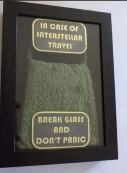 A framed green towel is displayed behind glass, with two yellow text boxes overlaid. The top box reads 'IN CASE OF…
