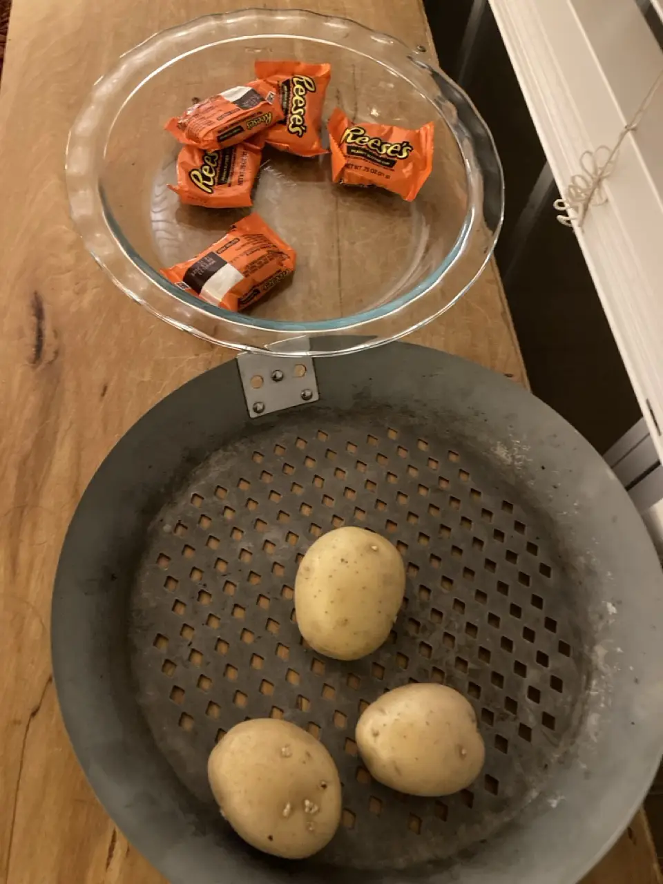A clear glass pie dish containing several orange-wrapped Reese's peanut butter cups is balanced on top of a metal steamer…
