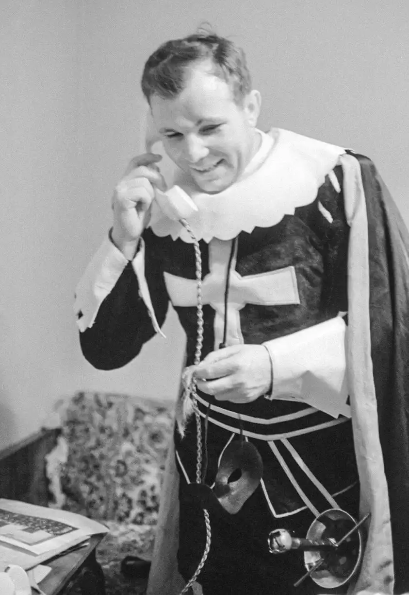 A black-and-white photo shows a man in a papal-style robe and white ruff collar holding a vintage telephone receiver to his…