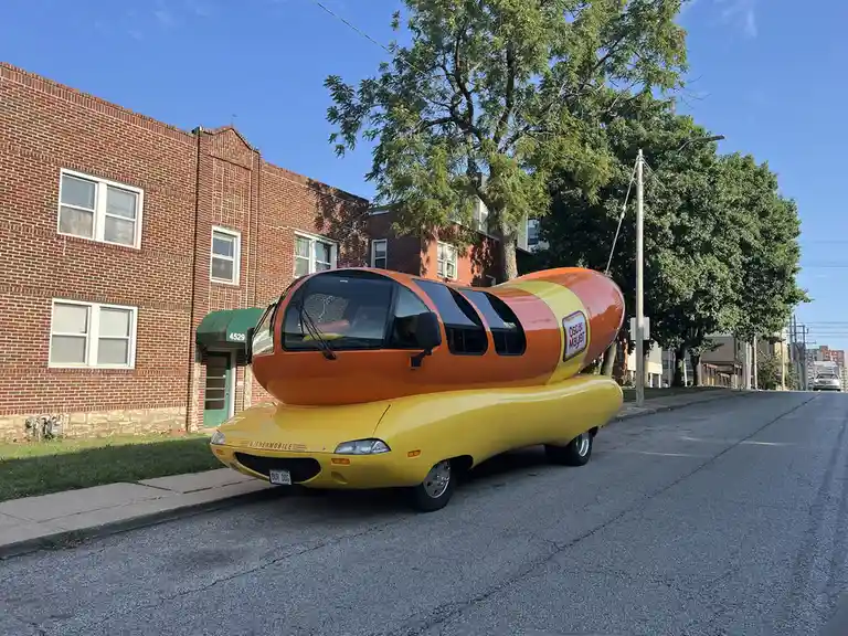 A bright yellow and orange car shaped like a hot dog with the 'Oscar Mayer' logo on its side is parked on a residential…
