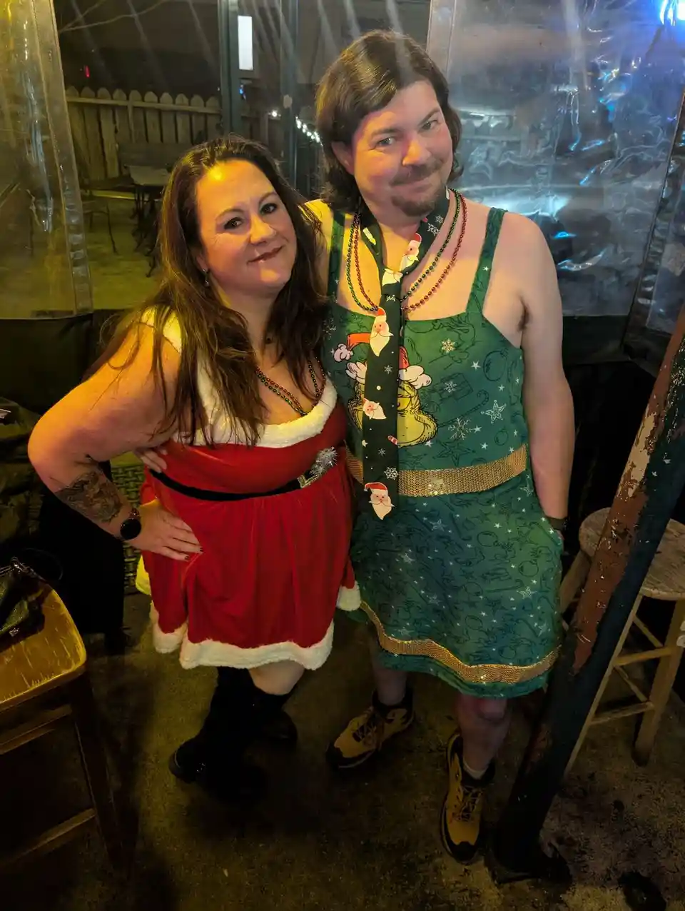A man and a woman pose together at what appears to be a festive event, both dressed in holiday-themed outfits. The woman…