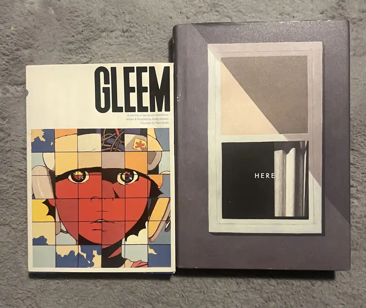 Two books lie side by side on a gray textured surface. The left book has a colorful, pixelated cover featuring a stylized…
