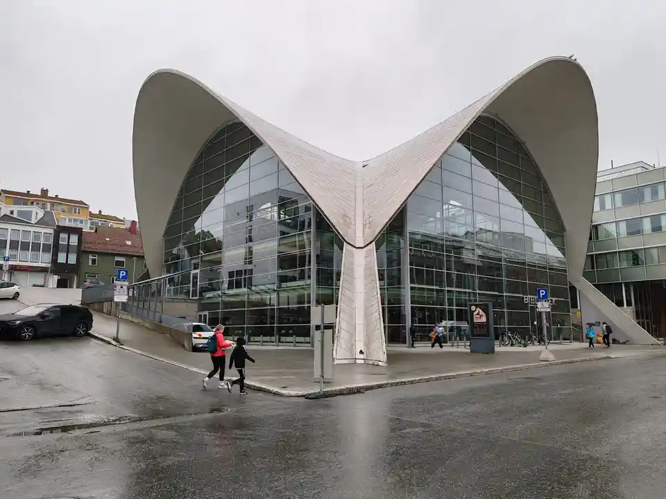 A wide shot of a modern, architecturally striking building with two large, curved, wing-like concrete structures flanking a…