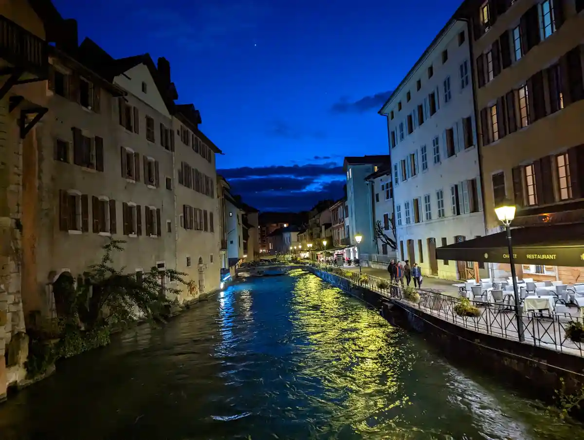 A serene night scene of a European canal flanked by old buildings with lit windows and street lamps casting golden…
