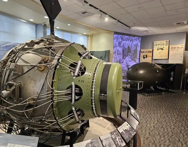 A large, exposed, olive-drab nuclear bomb casing labeled 'F41' is displayed in a museum, surrounded by wires and bolts, with…