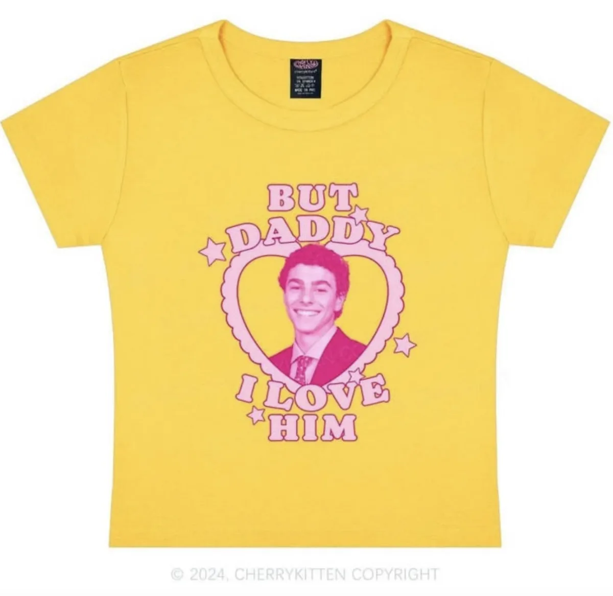 A bright yellow t-shirt features a pink graphic with the text 'BUT DADDY I LOVE HIM' surrounding a heart-shaped portrait of…