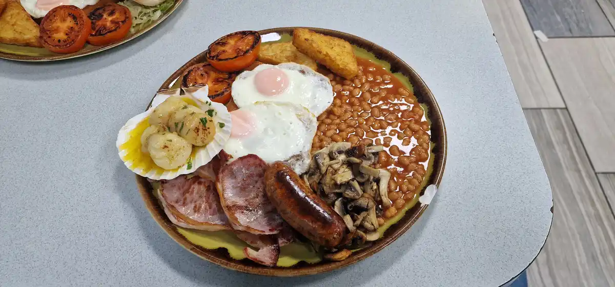 A plate of a traditional full English breakfast featuring fried eggs, baked beans, sausages, bacon, mushrooms, grilled…
