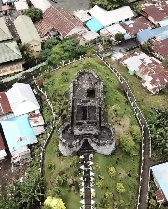 An aerial view shows a dilapidated, oddly shaped stone structure resembling a giant, broken toilet with a seat and bowl…