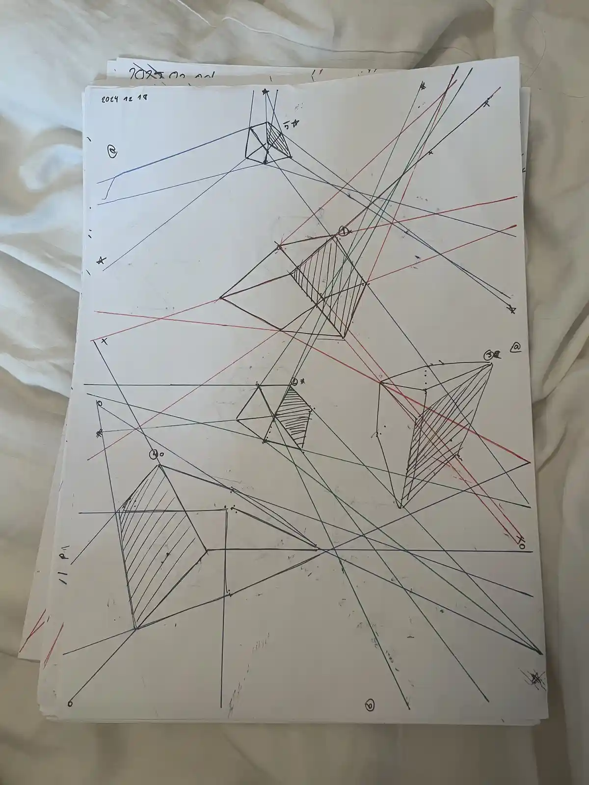 A close-up photo of a white sheet of paper covered in complex, overlapping geometric drawings in red, blue, and green ink…
