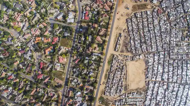 An aerial view shows a stark contrast between two neighborhoods divided by a road: one side features spacious…
