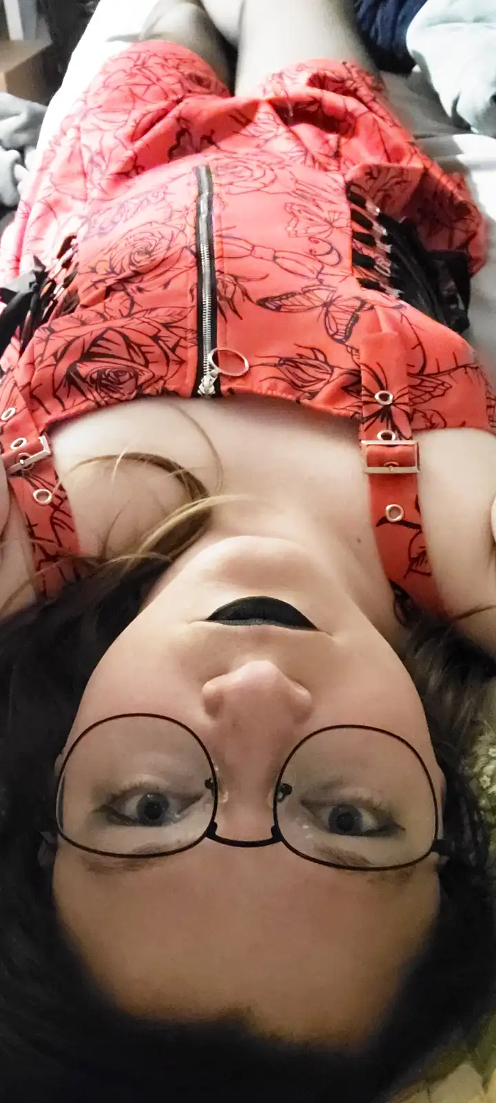 A person is lying on their back, looking up at the camera with a surprised or tired expression. They are wearing a red…