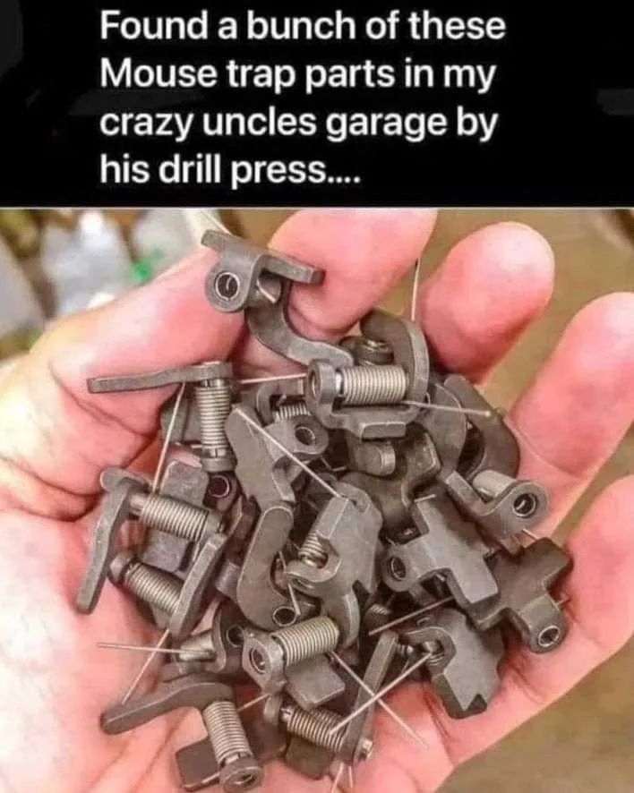 A hand holds a pile of small, identical metal components with springs and thin metal pins, which are parts of mousetraps…