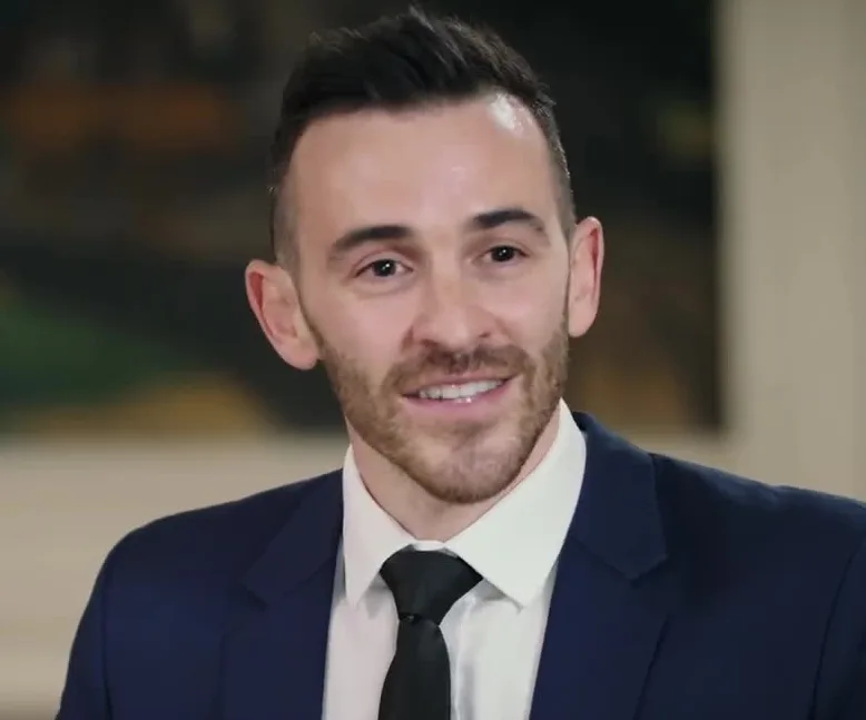 a man in a dark suit and black tie smiles confidently at the camera while overlaid text reads 'i'm not a fan of the new…