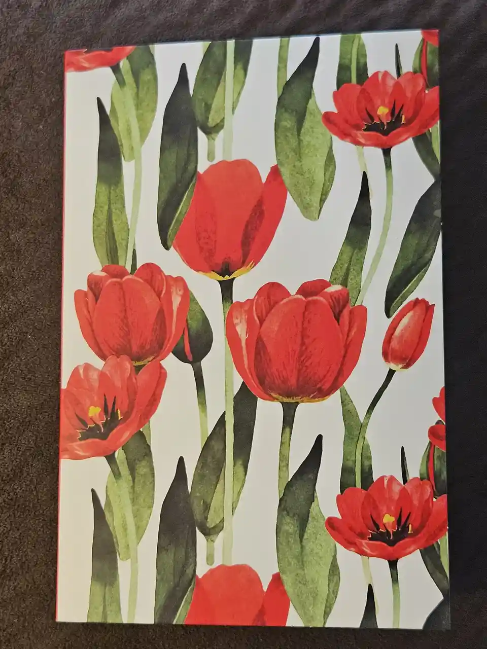 A printed image of red tulips with green stems and leaves on a light background, overlaid with the text 'i'm not a tulip…