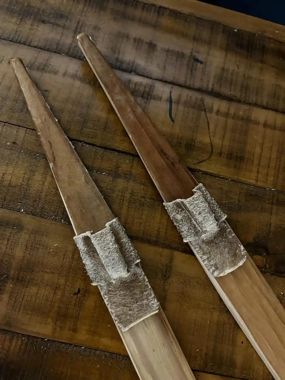 Two wooden sticks with rough, fibrous white material glued to their ends lie diagonally on a dark wooden surface. The…