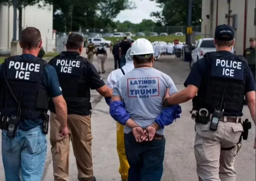 Four police officers labeled 'POLICE ICE' are escorting a man in a white hard hat and a gray t-shirt that reads 'LATINOS FOR…