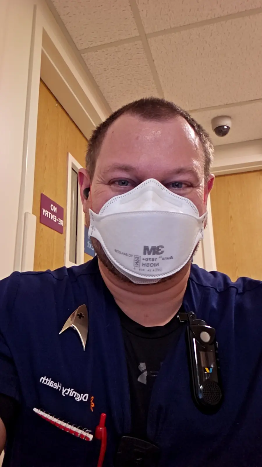 A man in blue medical scrubs with a 'Dignity Health' logo and a Star Trek captain's insignia pinned to his left chest…