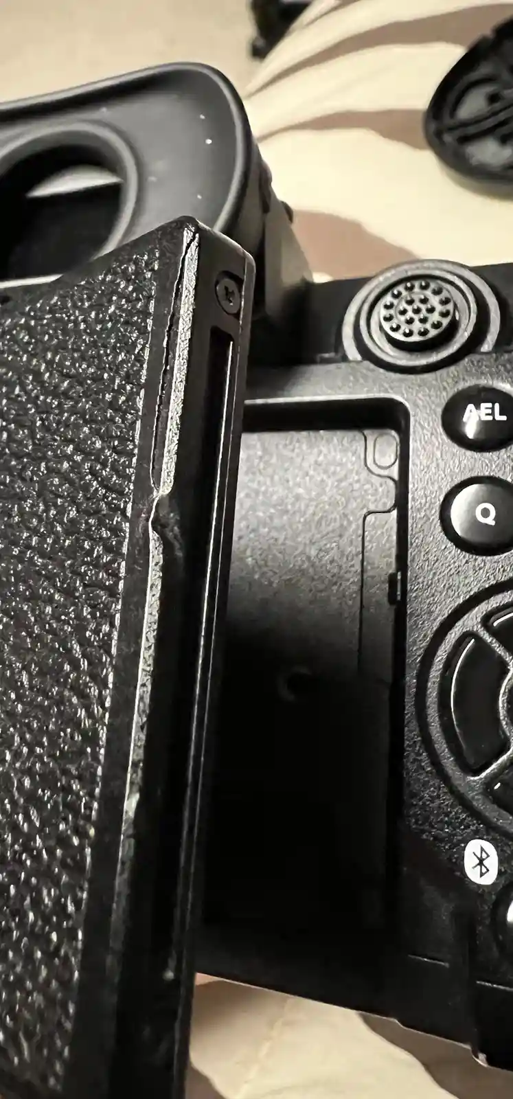 A close-up photo of a black DSLR camera's grip and top panel, showing a visible crack running vertically along the edge…