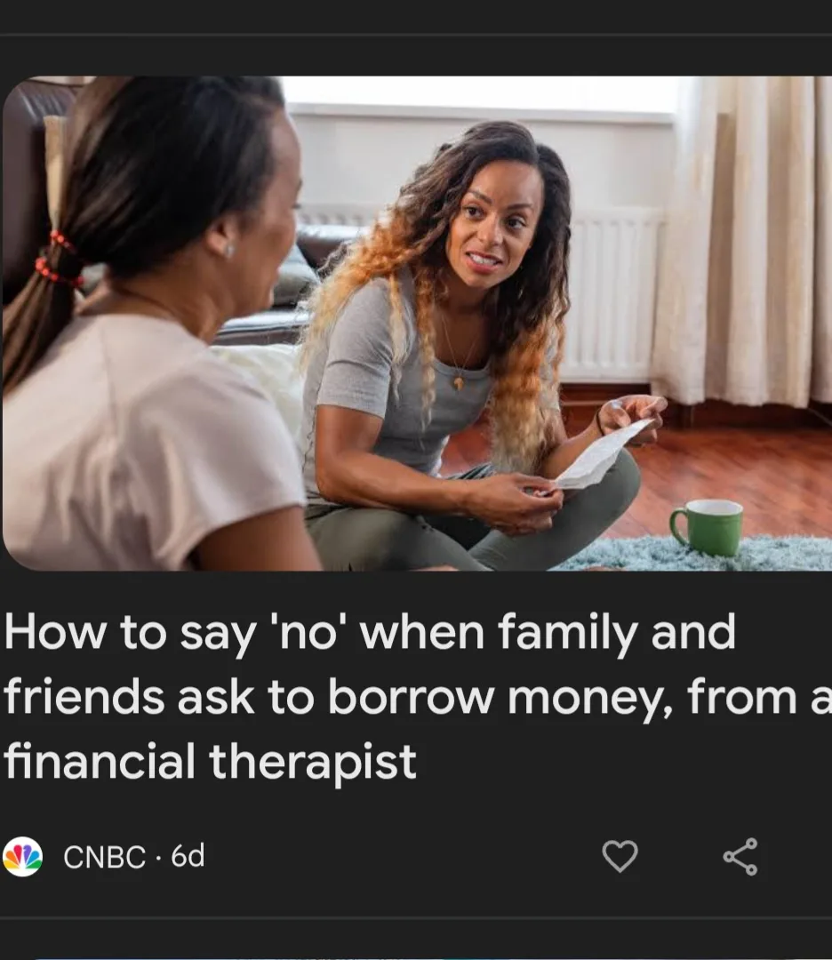 A woman with long curly hair sits on a rug holding a paper, smiling at another woman who is facing her. A green mug sits…