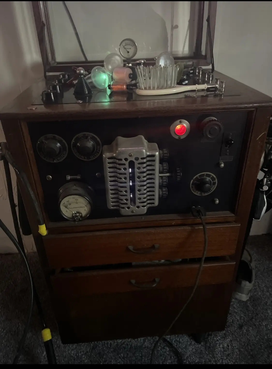 An old wooden cabinet with a glass-topped panel containing vintage electronic components like vacuum tubes, dials, and a…
