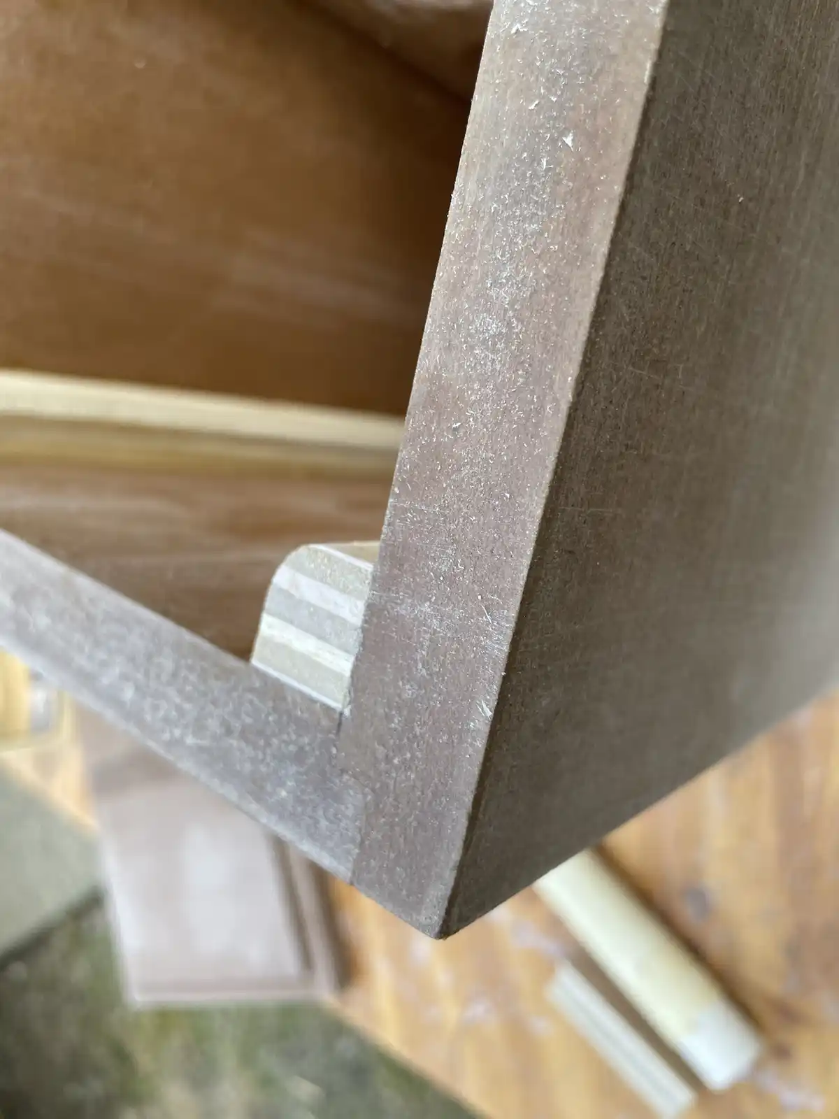 A close-up photo shows a handmade wooden corner joint, likely from a piece of furniture, with visible wood grain and dust…