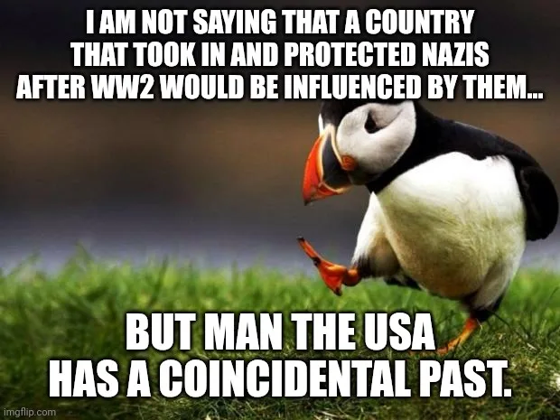 A penguin stands on grass, looking down with one foot lifted, as if in thought or mild embarrassment. The overlaid text…