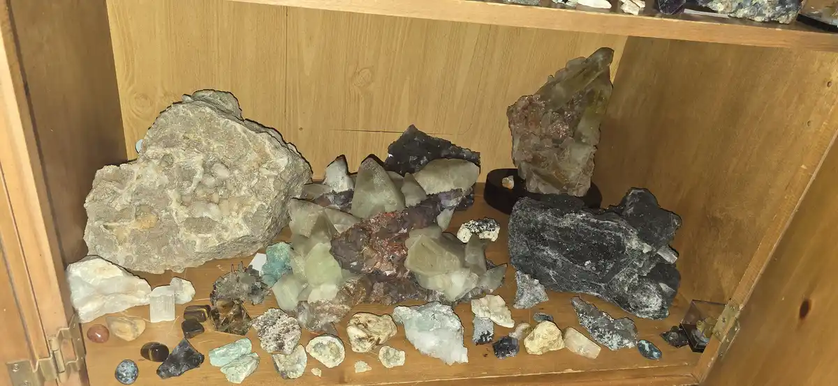 A wooden display case filled with various natural crystals and rocks of different sizes, shapes, and colors, including large…