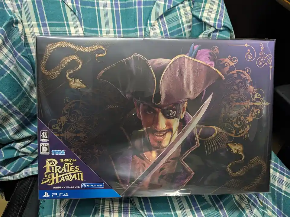 A person holds a sealed PlayStation 4 game box for 'Pirates in Hawaii,' featuring a pirate character with an eyepatch…