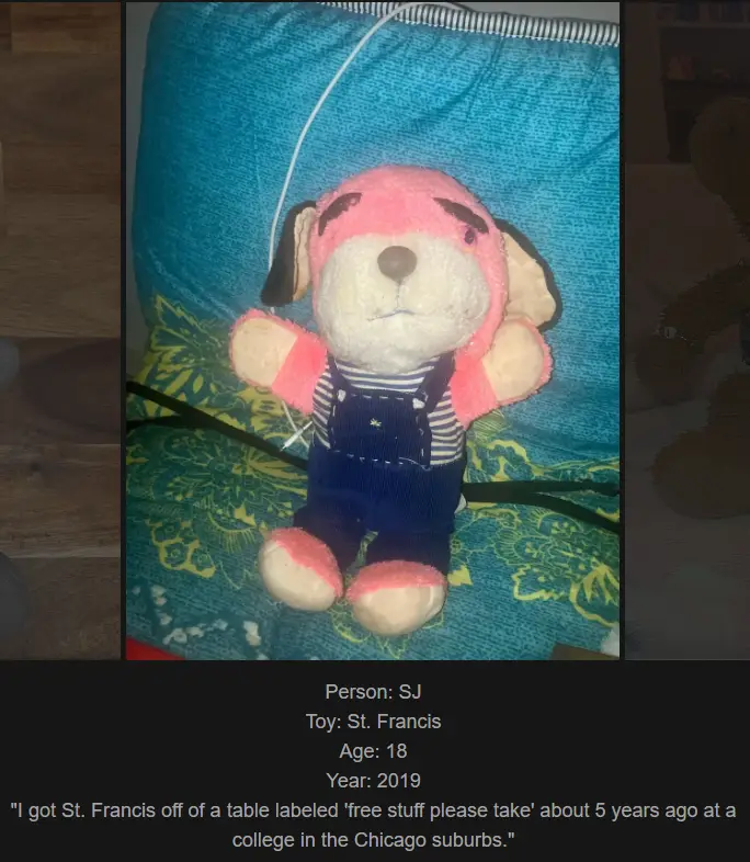 A pink plush dog toy named St. Francis, wearing blue overalls over a striped shirt, sits on a teal cushion with a yellow…