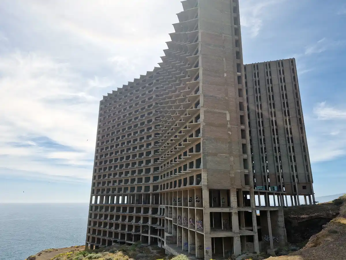 the image shows the partially constructed Hotel de la Costa, a striking abandoned concrete structure perched on a cliff…