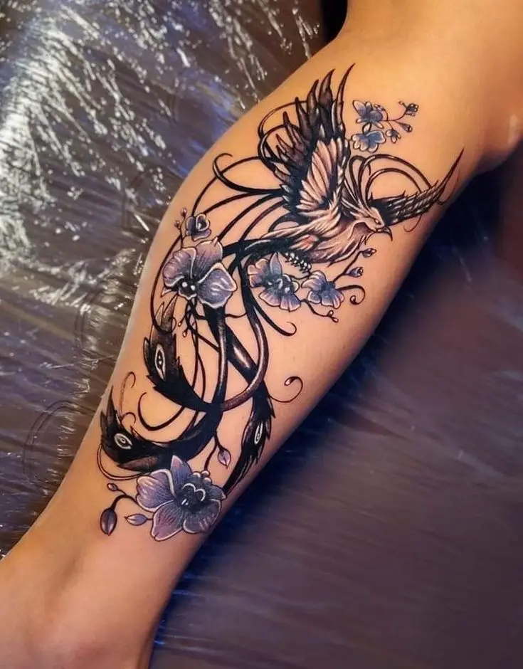 a close-up photo shows a detailed tattoo on a person's lower leg, featuring a stylized bird with outstretched wings…